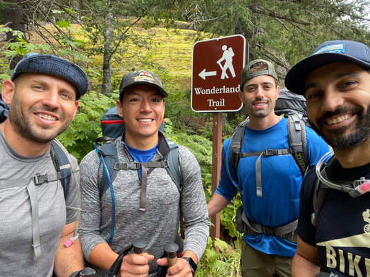 4 men in hiking gear with backpacks on standing in front of the entrance to the Wonderland Trail on Mt Rainier in Washington.
