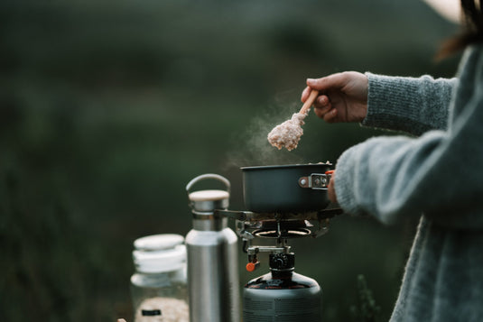 Person scooping outmeal from a pot outdoors over a gas camping stove.